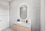 Floating vanity with wood-finish cabinetry, integrated countertop with an undermount sink, wall-mounted faucet, and oval backlit mirror set against te