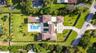 Aerial perspective featuring a multi-wing residence, expansive manicured lawn, paved driveway with geometric grid patterns, and an integrated swimming