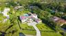 Aerial perspective of a multi-story residence featuring a tile roof, an expansive manicured lawn, a gated motor court, and a swimming pool