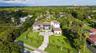 Two-story estate featuring a light-colored stucco exterior, multi-hipped tile roof, extensive lawn area, paved motor court, and mature palm landscapin