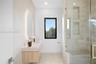 Floating wood-finish vanity with an integrated sink, illuminated oval wall mirror, walk-in shower with stone-tile surround, built-in shower niches, an