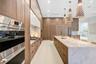 Kitchen featuring floor-to-ceiling wood-finish cabinetry, a large waterfall-edge stone island, professional-grade stainless steel wall ovens, a built-