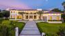 Contemporary residence featuring multi-level stone facade, floor-to-ceiling windows, tiled roof, linear paved driveway, and manicured landscaping