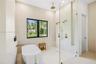 Freestanding soaking tub with wall-mounted faucet, walk-in shower featuring a frameless glass enclosure, gold-toned rainfall and handheld showerheads,