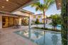 Covered outdoor patio with a natural wood-finish ceiling, stone tile flooring, built-in recessed lighting, integrated swimming pool, and landscaping