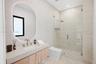 Floating wood-finish vanity with an integrated basin, backlit oval mirror, wall-to-wall stone-finish tiling, and a frameless glass-enclosed shower fea