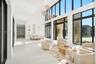 Expansive living area featuring vaulted ceilings, floor-to-ceiling windows with black frames, polished solid-surface flooring, and tiered multi-pendan