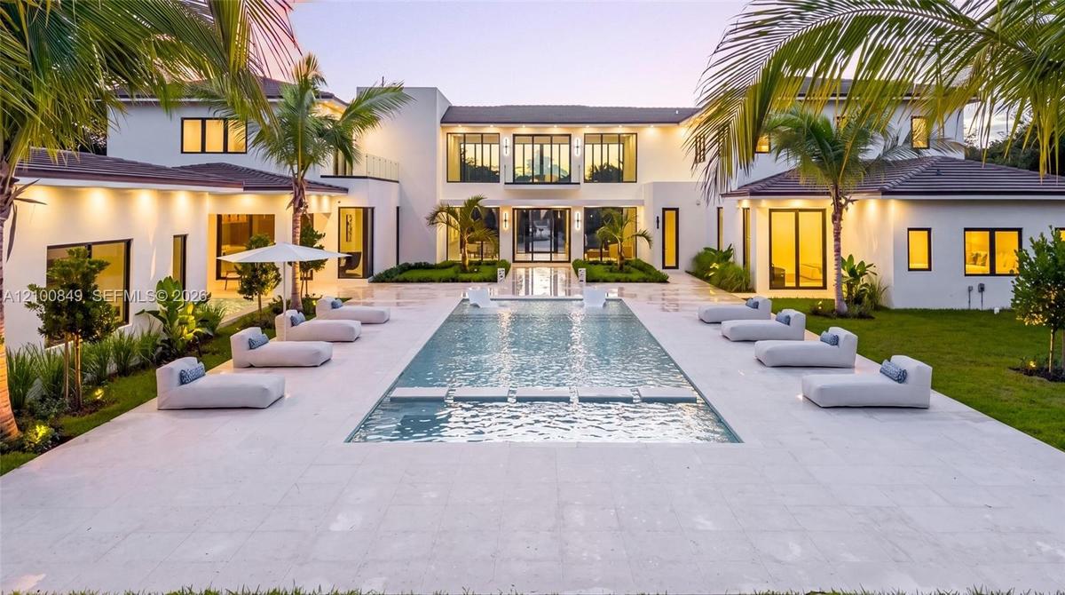 Contemporary estate exterior featuring a symmetrical stucco facade, expansive rectangular swimming pool with integrated stepping stones, wide stone-pa