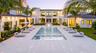 Contemporary estate exterior featuring a symmetrical stucco facade, expansive rectangular swimming pool with integrated stepping stones, wide stone-pa