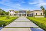 Contemporary residence featuring a stucco and stone exterior, two-story glass facade, expansive concrete driveway with inset greenery, and a multi-car
