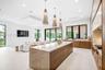 Chef's kitchen featuring a stone-topped waterfall island, custom wood cabinetry, recessed lighting, and trio of pendant light fixtures, finished with 