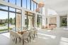 Double-height vaulted ceilings featuring expansive floor-to-ceiling windows, structured stone-clad accent wall, and polished concrete flooring