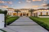 Contemporary two-story estate featuring a stone-clad exterior, floor-to-ceiling glass windows, a structured concrete paver driveway, and a gated entra