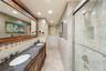 Double vanity with stone countertop, dual undermount sinks, intricate wood-finish cabinetry, a large framed vanity mirror, and a tiled walk-in shower 