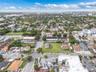 Aerial perspective of a corner lot featuring open, undeveloped green space, mature perimeter trees, and street-level access