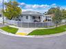 Single-story residence featuring a hipped roof, light-toned exterior finish, white metal perimeter fencing, and an attached carport