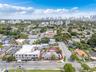 Aerial perspective of a corner lot property featuring a single-story residence with a concrete driveway and paved parking area
