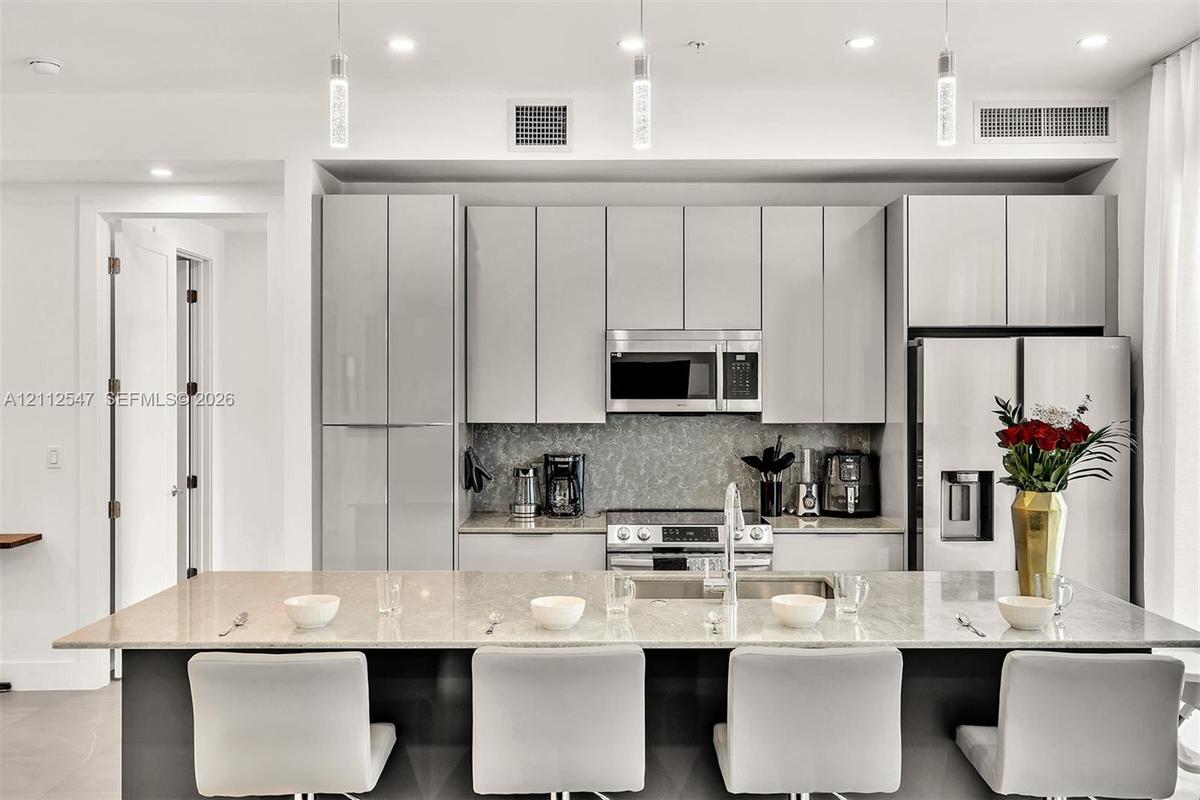 Kitchen featuring flat-panel cabinetry, a stone-surfaced kitchen island, stainless steel appliances, and glass pendant lighting