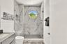 Walk-in shower featuring large-format patterned tile, glass enclosure, built-in bench, circular window, and handheld shower fixture