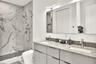 Bathroom featuring a dual-sink vanity with stone countertop, walk-in shower with floor-to-ceiling tile surround, glass partition, and wall-mounted lig