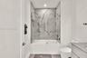 Full-height shower surround with veined tile, frameless glass enclosure, recessed shower niche, deep soaking tub, and stone-finish vanity countertop