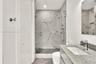 Bathroom featuring a walk-in shower with large-format stone-patterned tile, frameless glass enclosure, wall-mounted shower hardware, floating vanity w