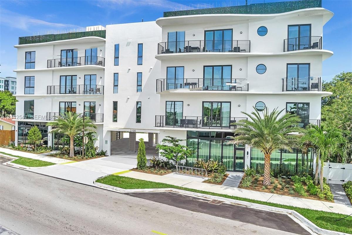Contemporary mid-rise exterior featuring smooth white stucco finish, wraparound balconies with metal railing, floor-to-ceiling glass windows, circular