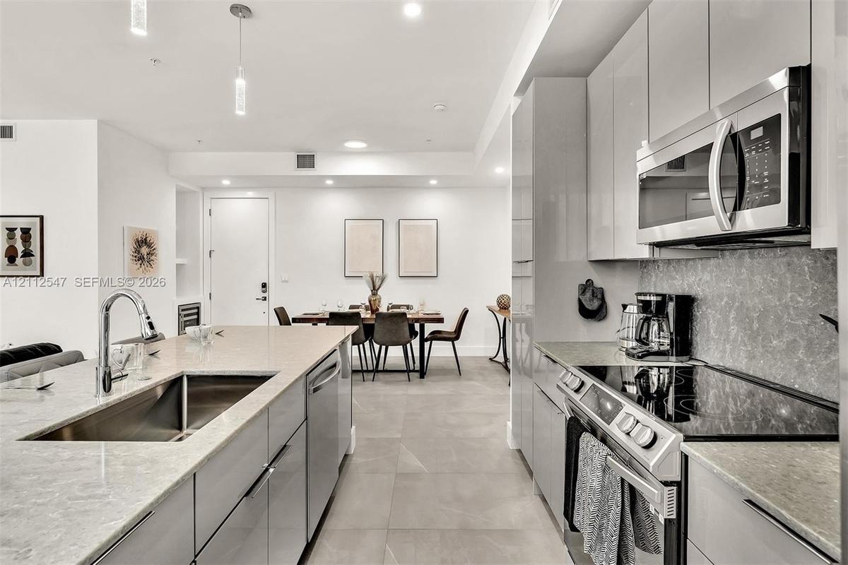 Kitchen featuring high-gloss cabinetry, stone-finish countertops, stainless steel appliances, large-format floor tile, and pendant lighting