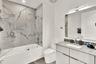 Bathroom featuring a tub-shower combination with floor-to-ceiling large-format tile surround, a glass shower panel, a floating vanity with a stone cou