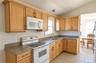 Kitchen featuring natural wood cabinetry, stone-finish countertops, tile flooring, and integrated white appliances