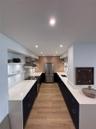 Kitchen featuring dark flat-panel cabinetry, light-toned stone countertops, wood-finish flooring, stainless steel appliances, and integrated recessed 