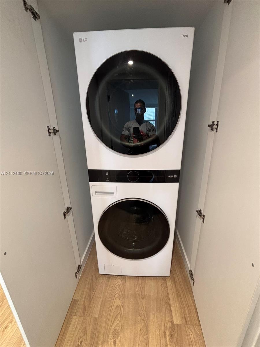 Stacked laundry unit featuring a white finish, circular glass-front doors, integrated digital control panels, and light-toned wood-finish flooring