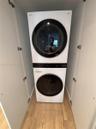 Stacked laundry unit featuring a white finish, circular glass-front doors, integrated digital control panels, and light-toned wood-finish flooring