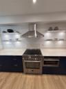 Kitchen featuring dark flat-panel cabinetry, quartz countertops, a stainless steel range with a matching chimney-style hood, and integrated under-shel