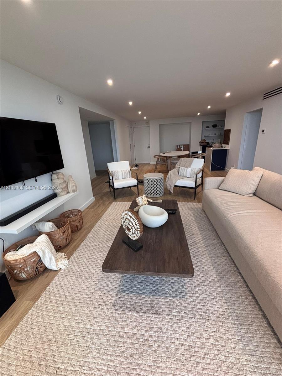 Living area featuring wood-finish flooring, recessed lighting, and a wall-mounted shelving unit