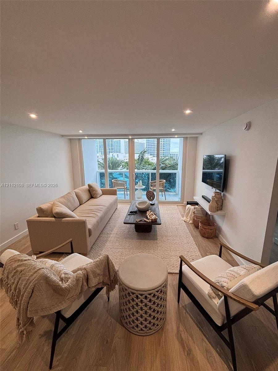 Living area featuring wood-finish flooring, recessed lighting, and floor-to-ceiling glass doors providing balcony access
