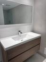 Floating vanity featuring a wood-finish cabinet with dual drawers, integrated white sink, polished chrome faucet, and large wall-mounted mirror agains