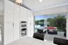 Floor-to-ceiling high-gloss cabinetry featuring an integrated stainless steel double oven and microwave, stone-finish island, and large glass sliding 