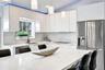 Kitchen featuring white high-gloss cabinetry, stone countertops with matching backsplash, central island, stainless steel refrigerator, and pendant li