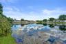 Waterfront lot featuring a natural pond, mature trees, and expansive shoreline grass