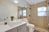 Bathroom featuring a vessel sink with a dark metal faucet, expansive vanity mirror, walk-in shower with floor-to-ceiling neutral tiling, and glass enc