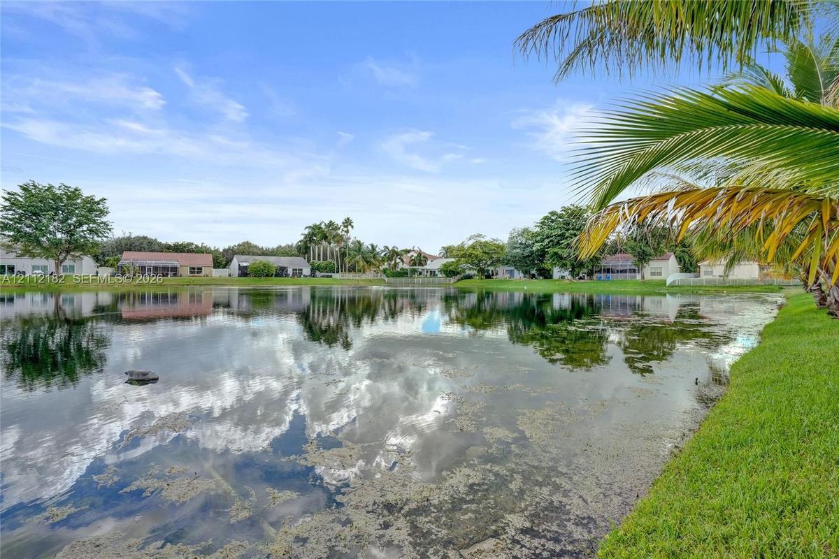 Waterfront property featuring a pond, manicured lawn, and mature palm trees