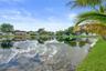Waterfront property featuring a pond, manicured lawn, and mature palm trees
