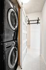 Stacked laundry units featuring a white sliding door with frosted glass panels and large-format tile flooring