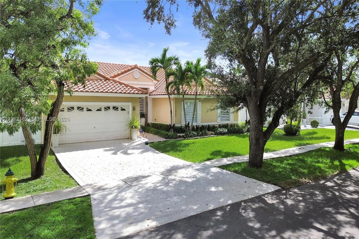 Single-story residence featuring a tiled roof, paver driveway, two-car garage, and established landscaping