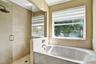 Walk-in shower with floor-to-ceiling tile, soaking tub with surround tiling, frameless glass enclosure, and a window providing water exposure