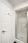 Walk-in shower featuring a glass door, textured wall tile, a rainfall showerhead, and a satin-finish lever handle