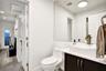 Bathroom vanity featuring a vessel sink, dark cabinetry, and a large-format wall mirror, complemented by wood-finish flooring and a single-piece toile
