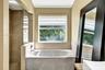 Soaking tub with a stone-finish surround, walk-in shower with floor-to-ceiling tile, and large window with exterior water backdrop