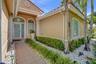 Stucco exterior with tile roof, tiled entryway, glass-paneled front door with arched transom window, and landscaped stone garden beds